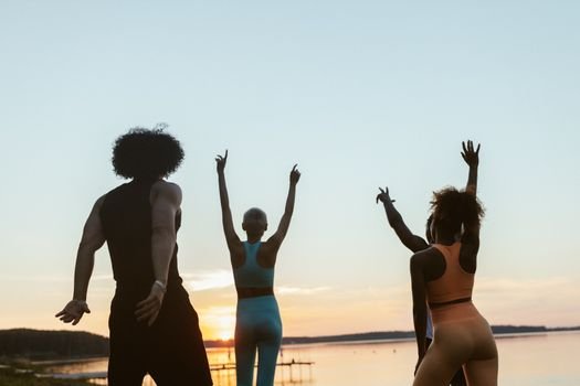 Group of diverse individuals exercising at sunset by a lake, embracing fitness and nature.